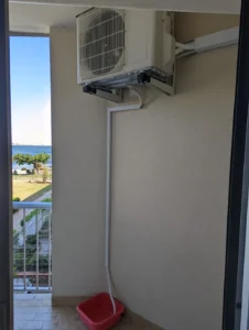 Unité extérieure d’une clim réversible fixée au mur d’un balcon avec évacuation des condensats