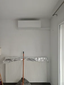 Unité murale de climatisation réversible fraîchement posée au-dessus d’un radiateur protégé pendant les travaux