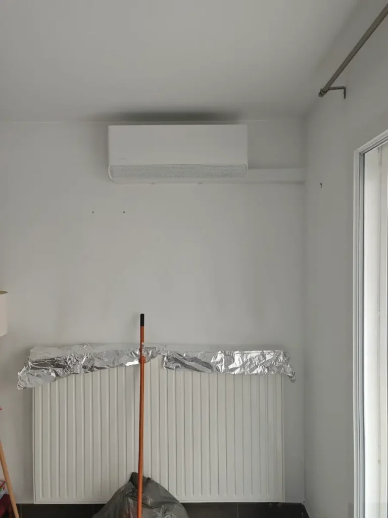 Unité murale de climatisation réversible fraîchement posée au-dessus d’un radiateur protégé pendant les travaux
