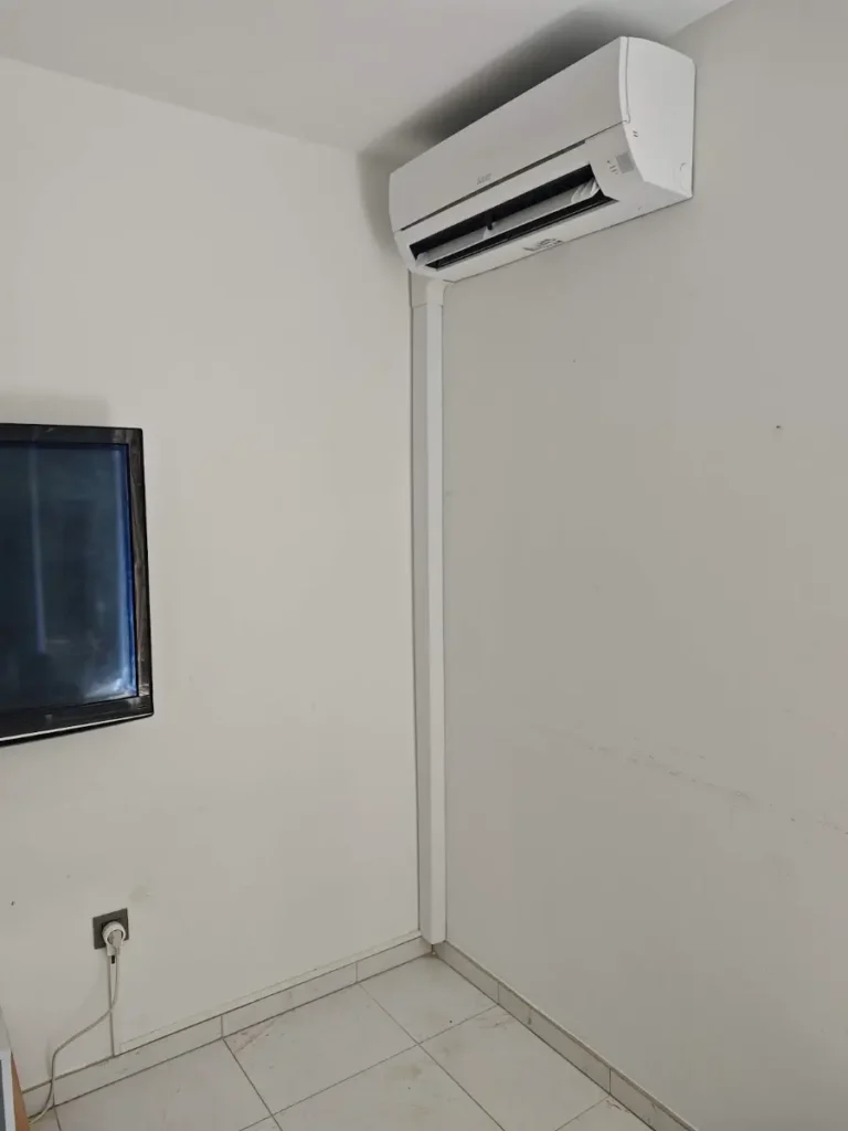 Unité murale de climatisation dans le séjour d’un appartement, goulotte blanche discrète le long du mur