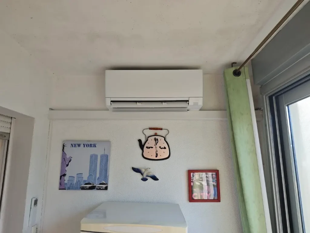 Unité murale de climatisation réversible installée dans une chambre, au-dessus de la tête de lit