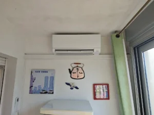 Unité murale de climatisation réversible installée dans une chambre, au-dessus de la tête de lit