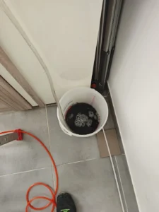 Seau recueillant l’eau de rinçage d’une clim, évacuation contrôlée lors d’une intervention pour fuite