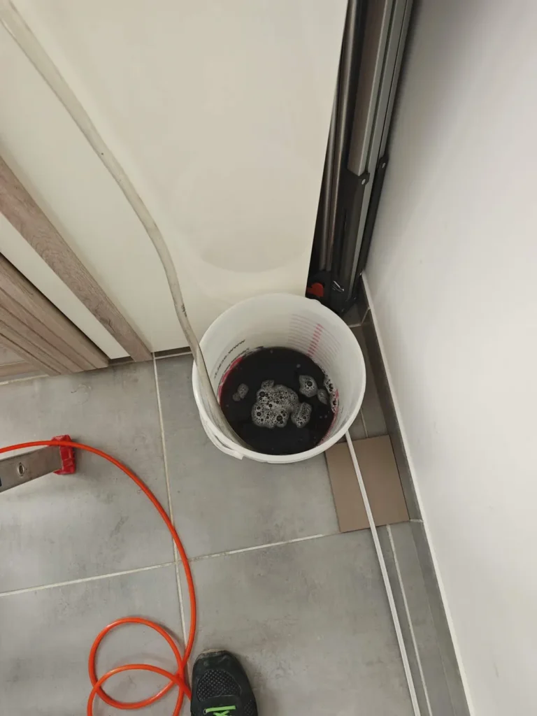 Seau recueillant l’eau de rinçage d’une clim, évacuation contrôlée lors d’une intervention pour fuite