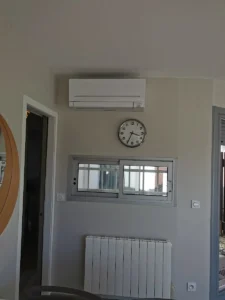 Unité murale de climatisation réversible installée au-dessus d’un radiateur électrique dans une pièce de vie