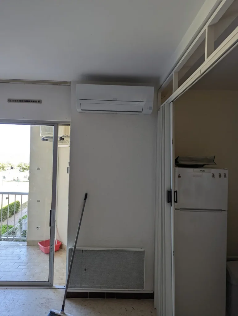 Unité intérieure murale installée au-dessus d’une porte dans une pièce de vie ouverte sur le balcon