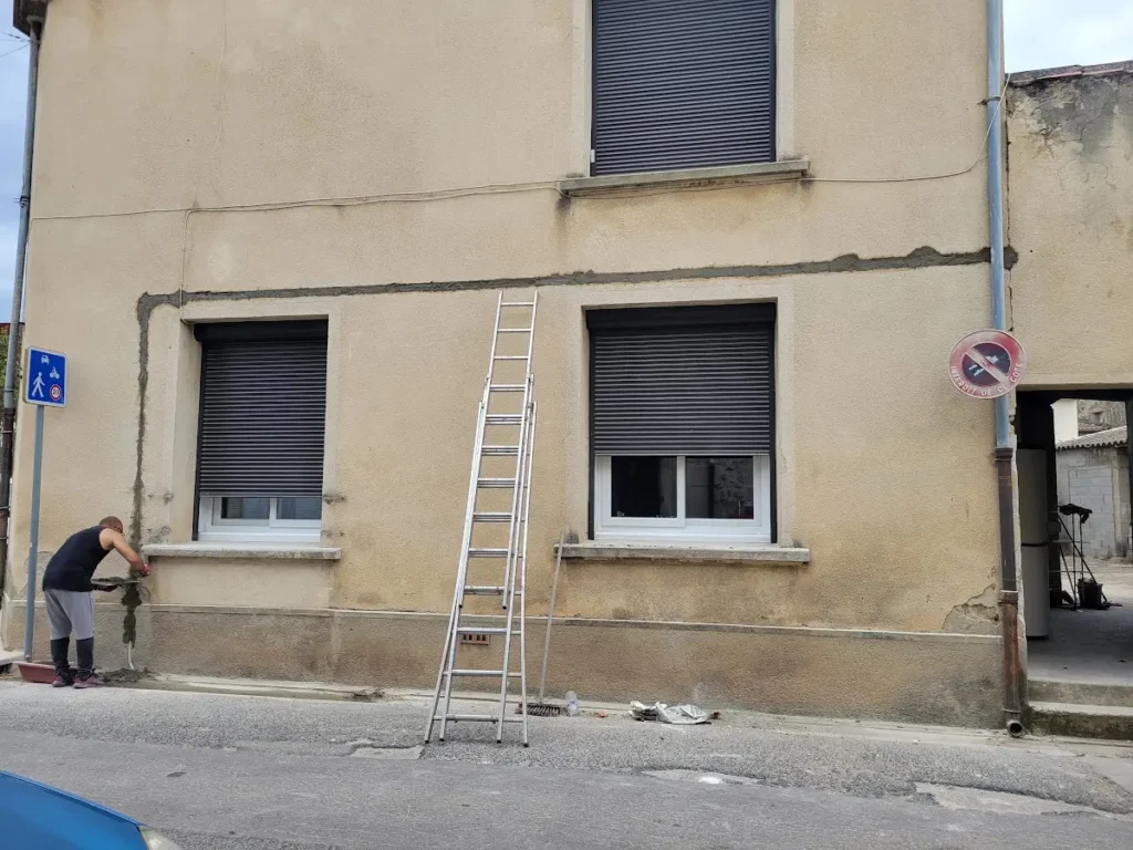 Façade enduite d’une maison de village pendant une intervention, échelle posée contre le mur