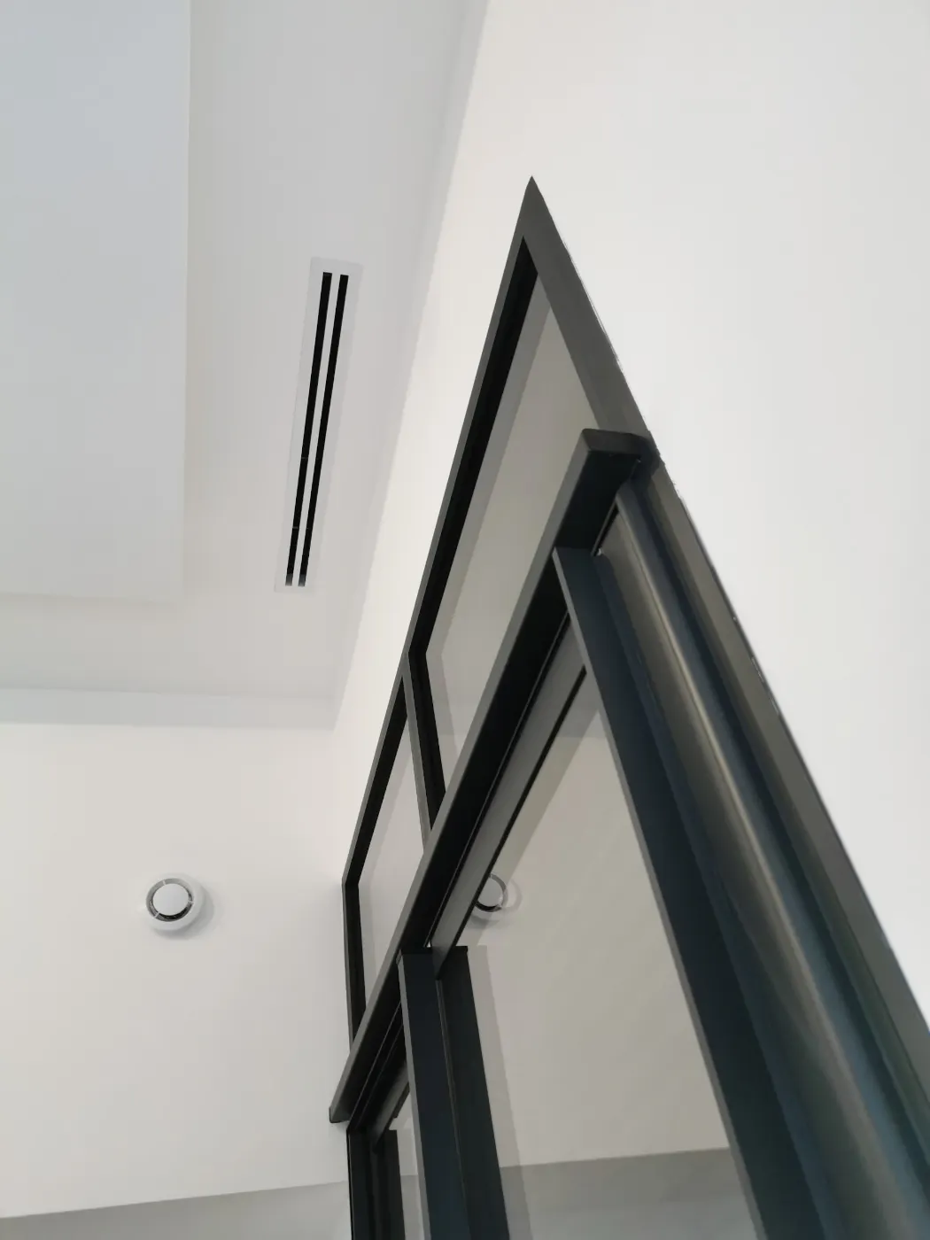 Grille de soufflage d’une climatisation intégrée au plafond près d’une baie vitrée