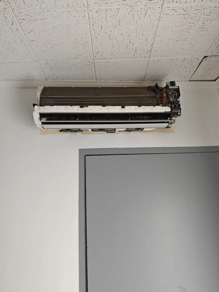 Unité murale de climatisation démontée pour un nettoyage complet au-dessus d’une porte de bureau