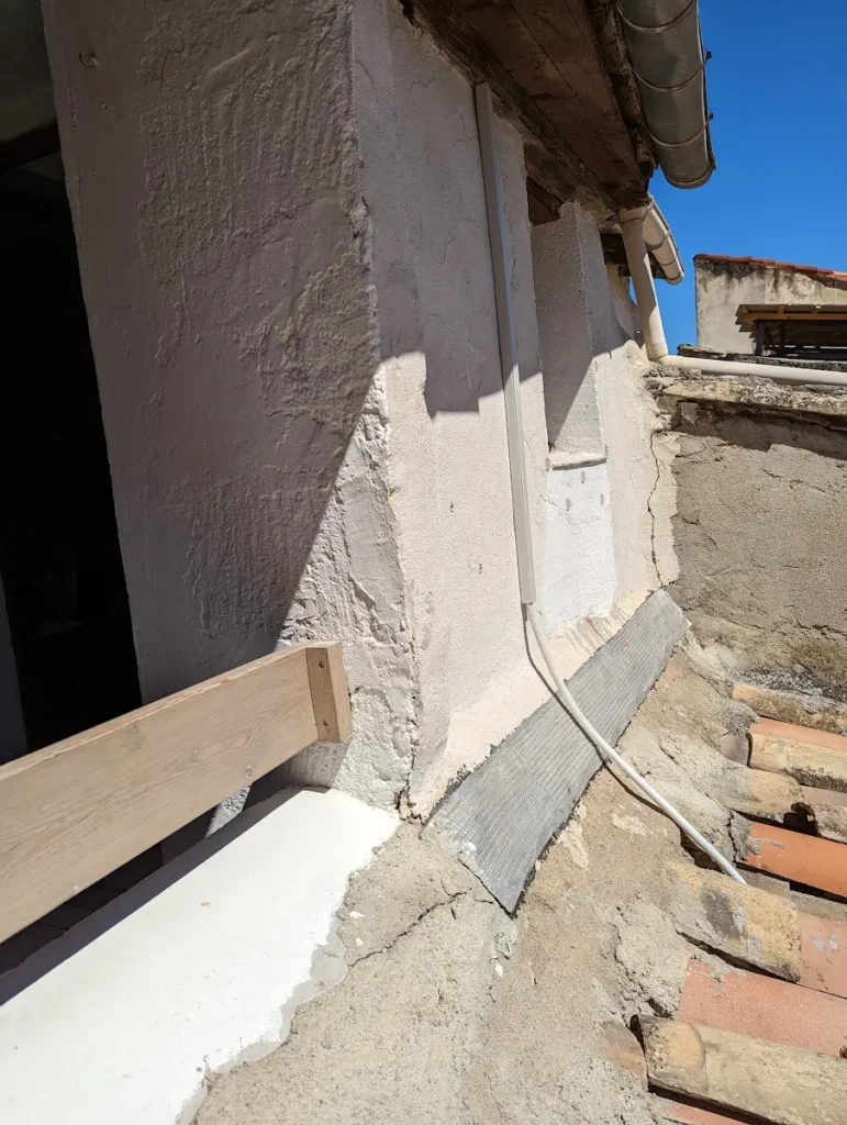 Liaisons frigorifiques protégées le long d’un mur ancien enduit, au ras d’une toiture en tuiles