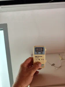 Frigoriste mesurant la température de l’air soufflé par une climatisation réversible avec un thermomètre