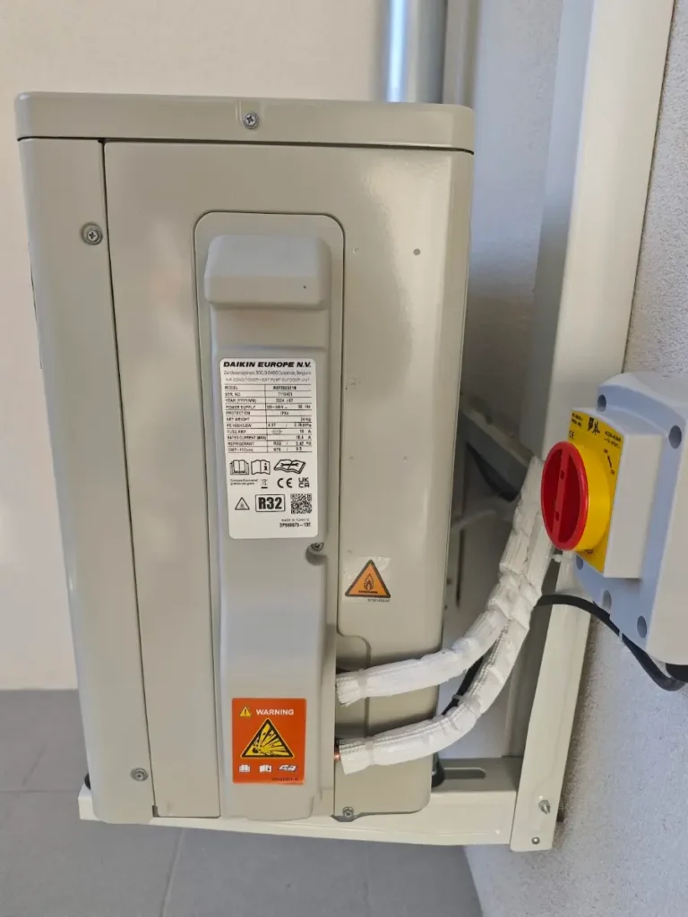 Unité extérieure Daikin fixée en façade, avec son interrupteur de proximité rouge et jaune