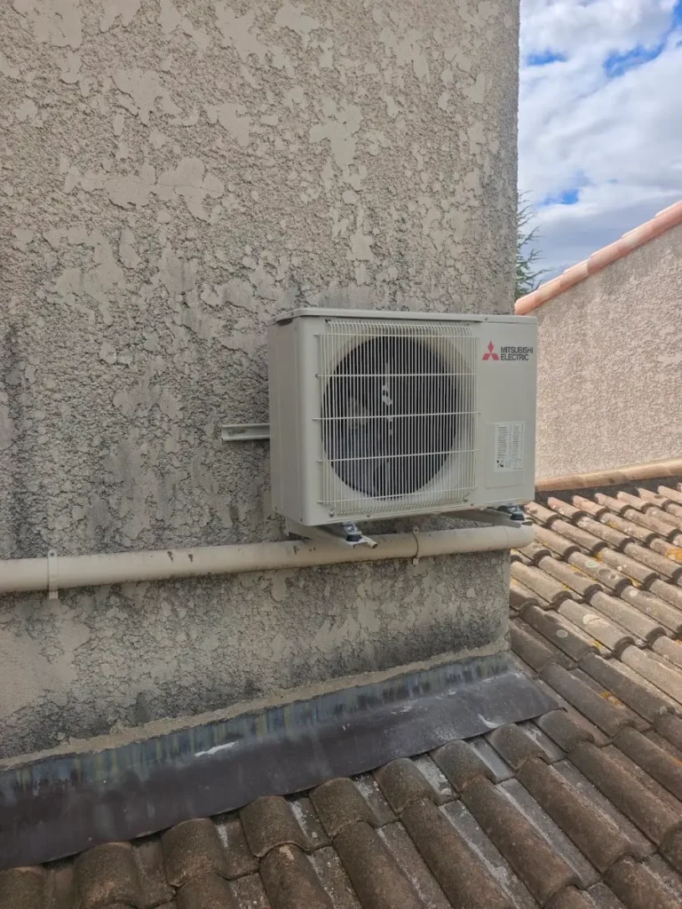 Unité extérieure Mitsubishi Electric fixée en façade au-dessus d’une toiture en tuiles canal