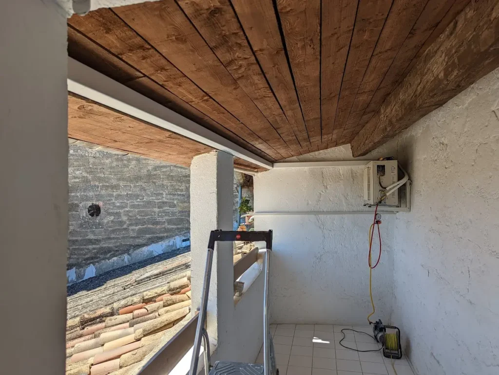 Unité extérieure de climatisation fixée dans une loggia sous plafond en bois d’une maison de village