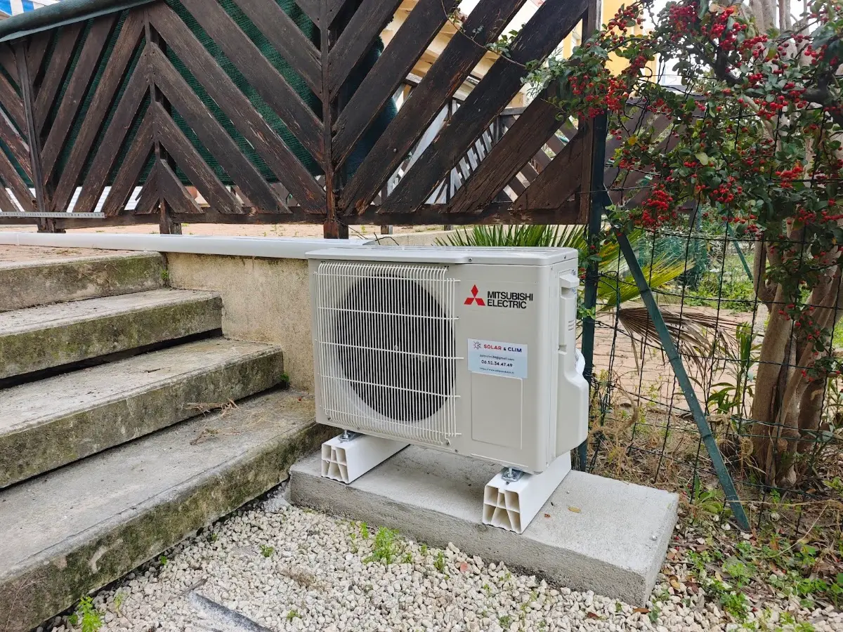 Unité extérieure de climatisation posée sur des plots anti-vibration dans un jardin : elle abrite le compresseur et le condenseur