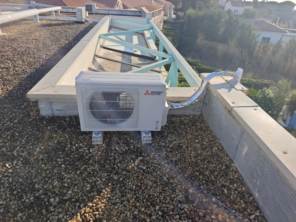 Unité extérieure Mitsubishi Electric posée sur plots au milieu d’un toit plat, à distance des fenêtres