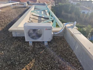 Unité extérieure Mitsubishi Electric posée sur plots au milieu d’un toit plat, à distance des fenêtres