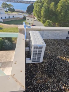 Unité extérieure de climatisation sur un toit-terrasse gravillonné, avec un étang littoral en arrière-plan