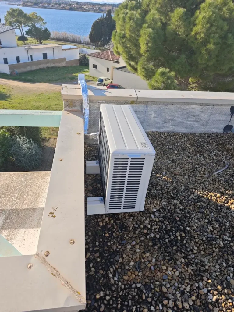 Unité extérieure de climatisation sur un toit-terrasse gravillonné, avec un étang littoral en arrière-plan