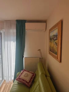 Unité intérieure murale de climatisation réversible posée en hauteur dans un salon, au-dessus d’un canapé