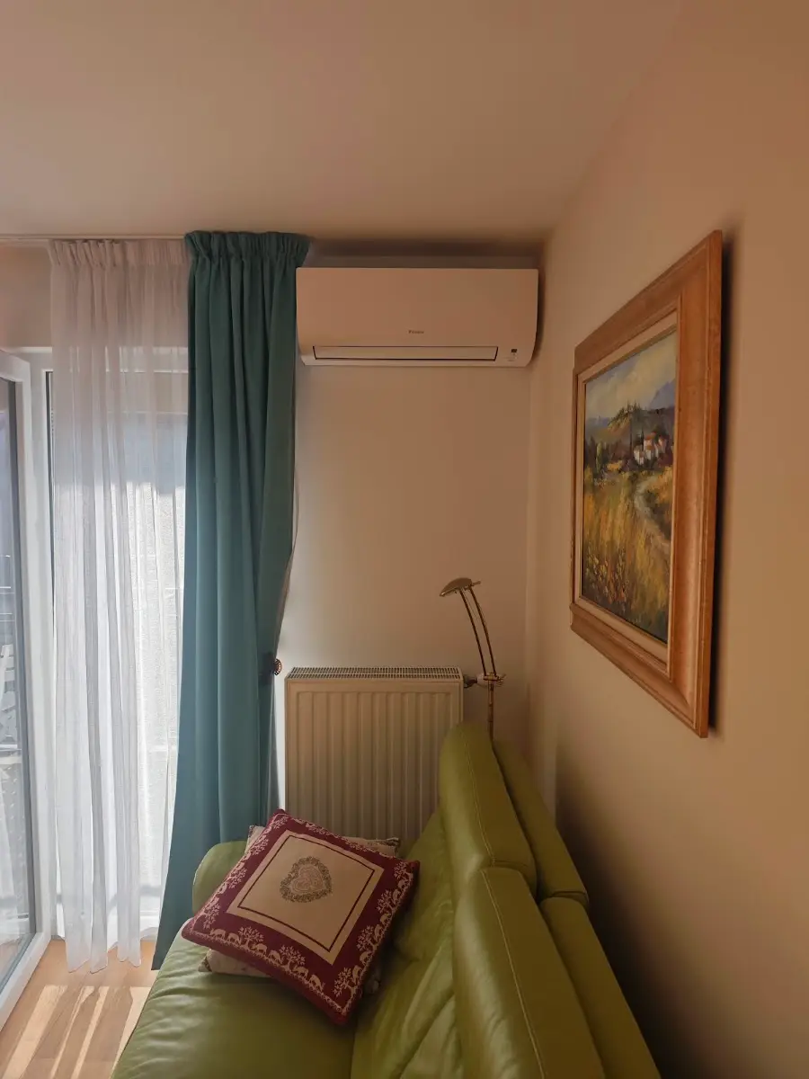 Unité intérieure murale de climatisation réversible posée en hauteur dans un salon, au-dessus d’un canapé