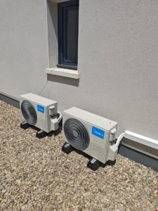 Deux unités extérieures de climatisation réversible posées sur plots anti-vibration sur le toit-terrasse gravillonné d’une maison neuve