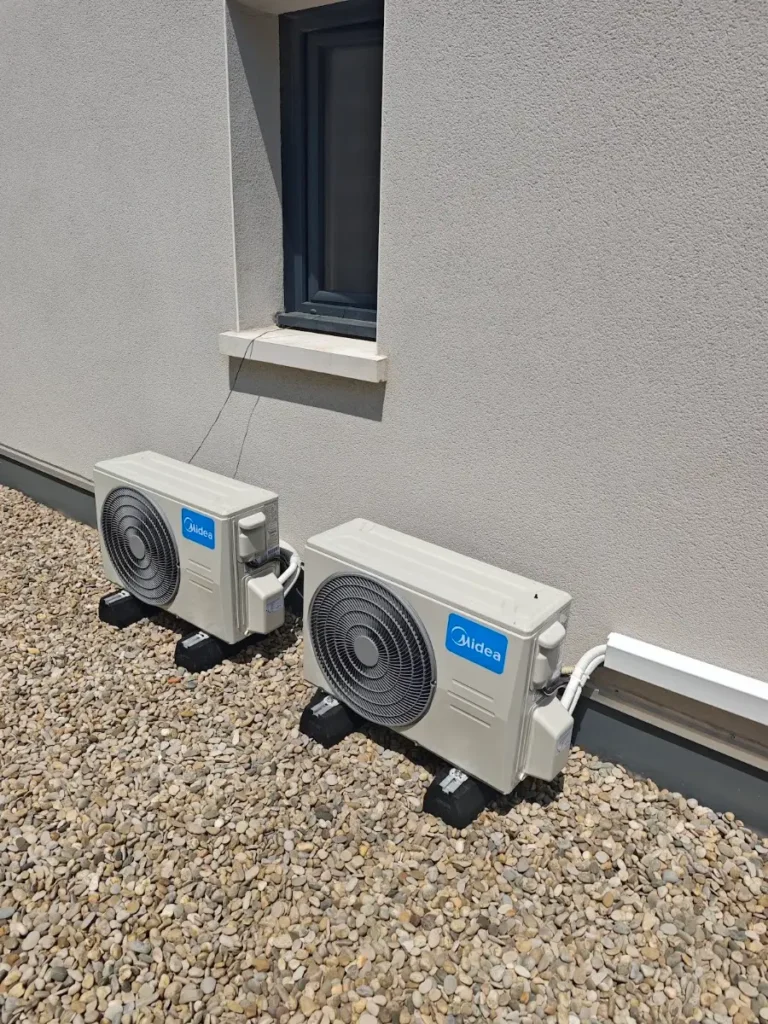 Deux unités extérieures de climatisation réversible posées sur plots anti-vibration sur le toit-terrasse gravillonné d’une maison neuve